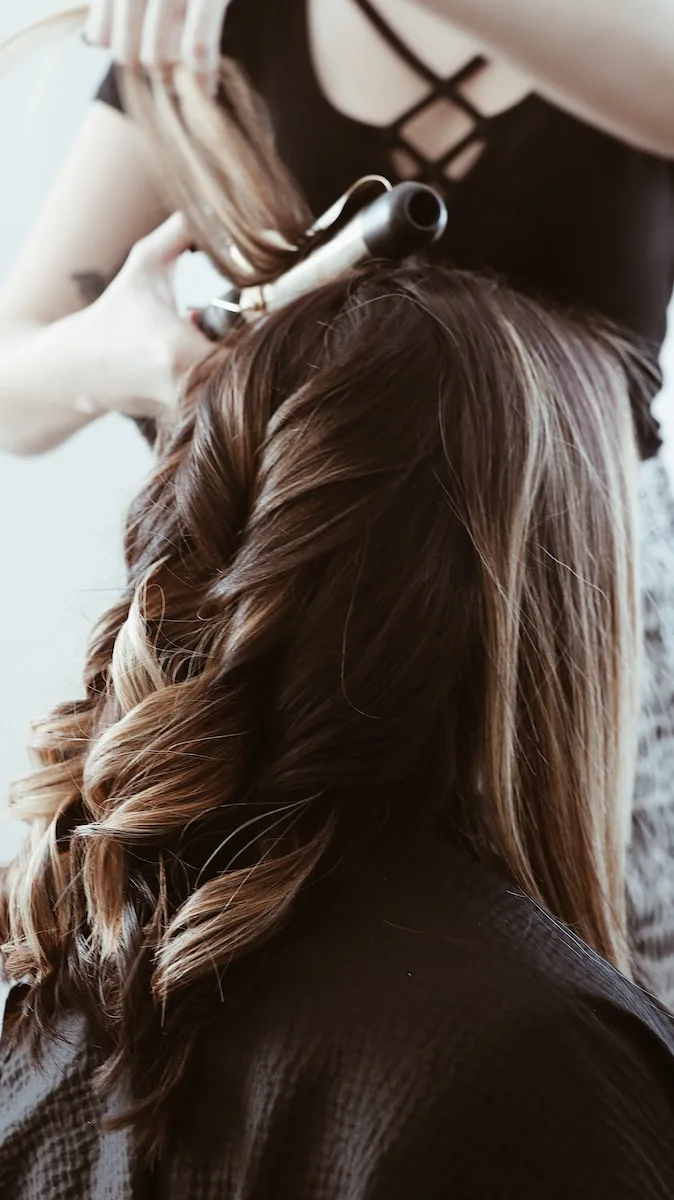 stylist curling dark blonde hair into waves with a curling iron